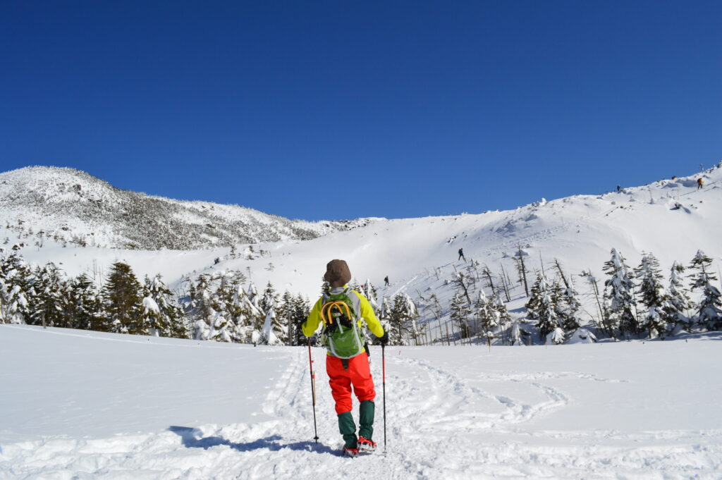 ワカンを背負って雪山登山に出発する男性の写真